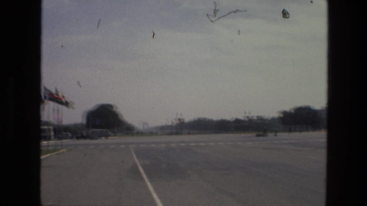 Open road beside a row of flags with lawns and a large distant building.