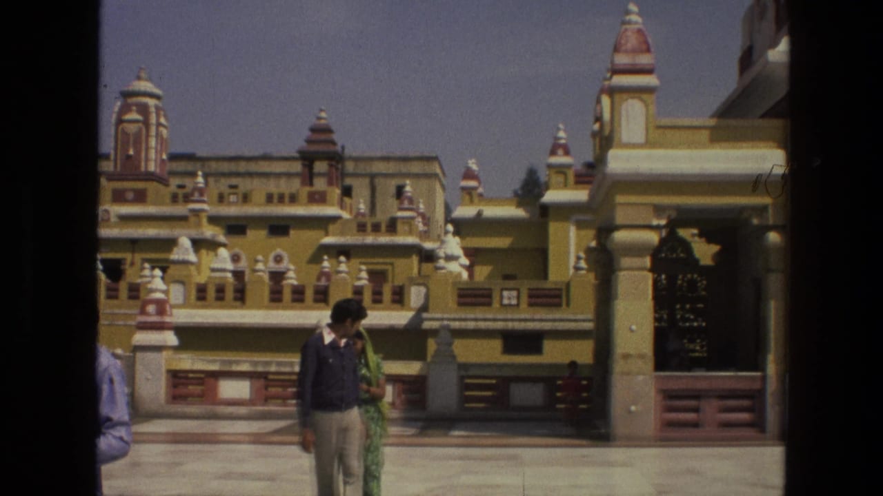 Man and woman walking across a courtyard in front of ornate yellow and red architecture.