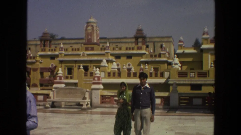 The couple continues across the courtyard in front of layered temple architecture, with another visitor partly visible at frame edge.