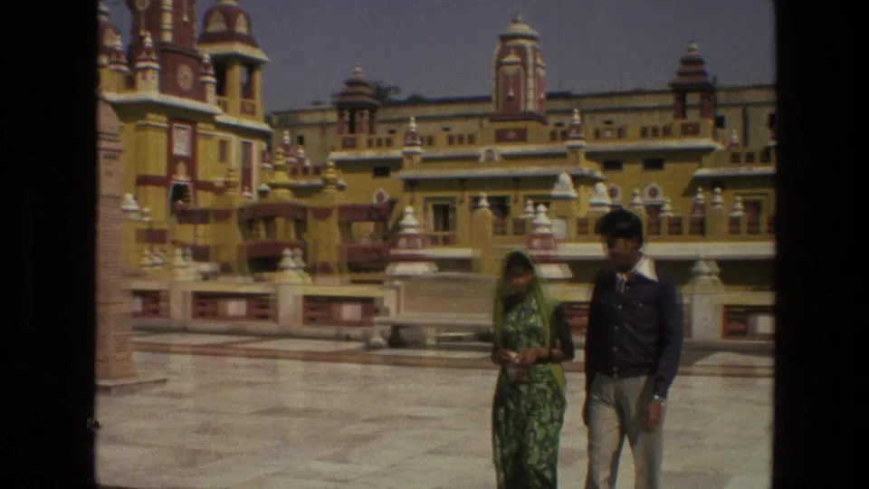 A man and woman walk through the temple courtyard as the 8mm frame shows dark gate borders and faded color.