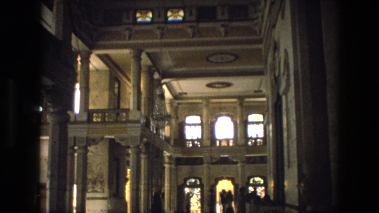 1974 India frame of a Rajput palace interior, with tall columns, arched windows, balcony details, and distant silhouetted visitors.