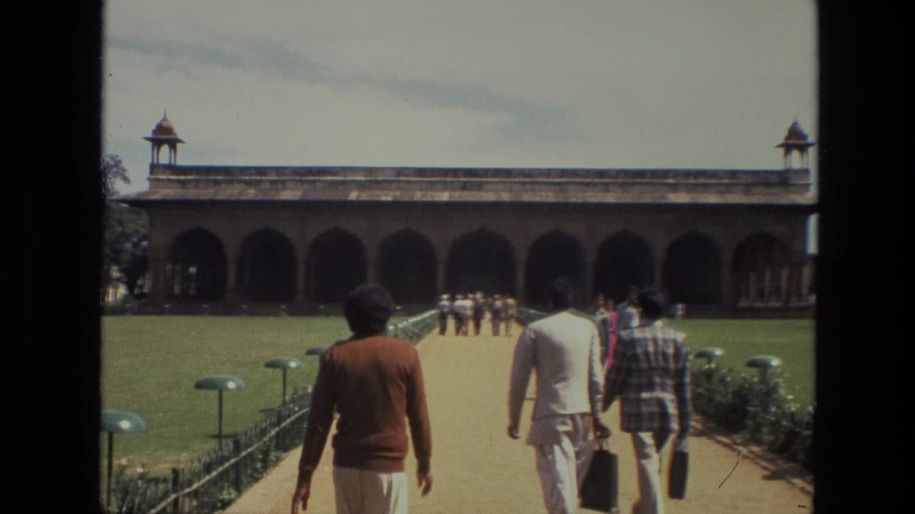 Several visitors walk away from the camera toward a large arched building.