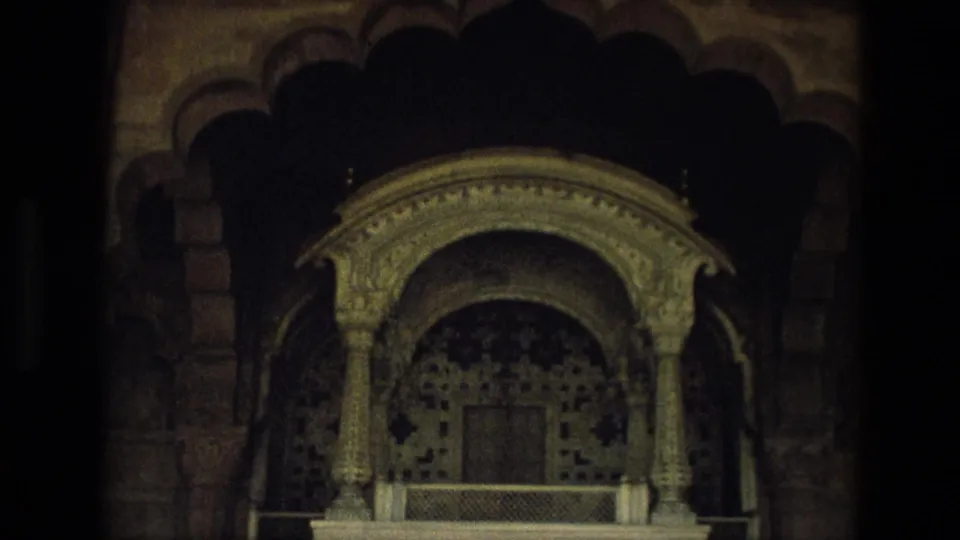 Interior 8mm frame from India showing a shadowed carved alcove with decorative stonework and scalloped arch forms.