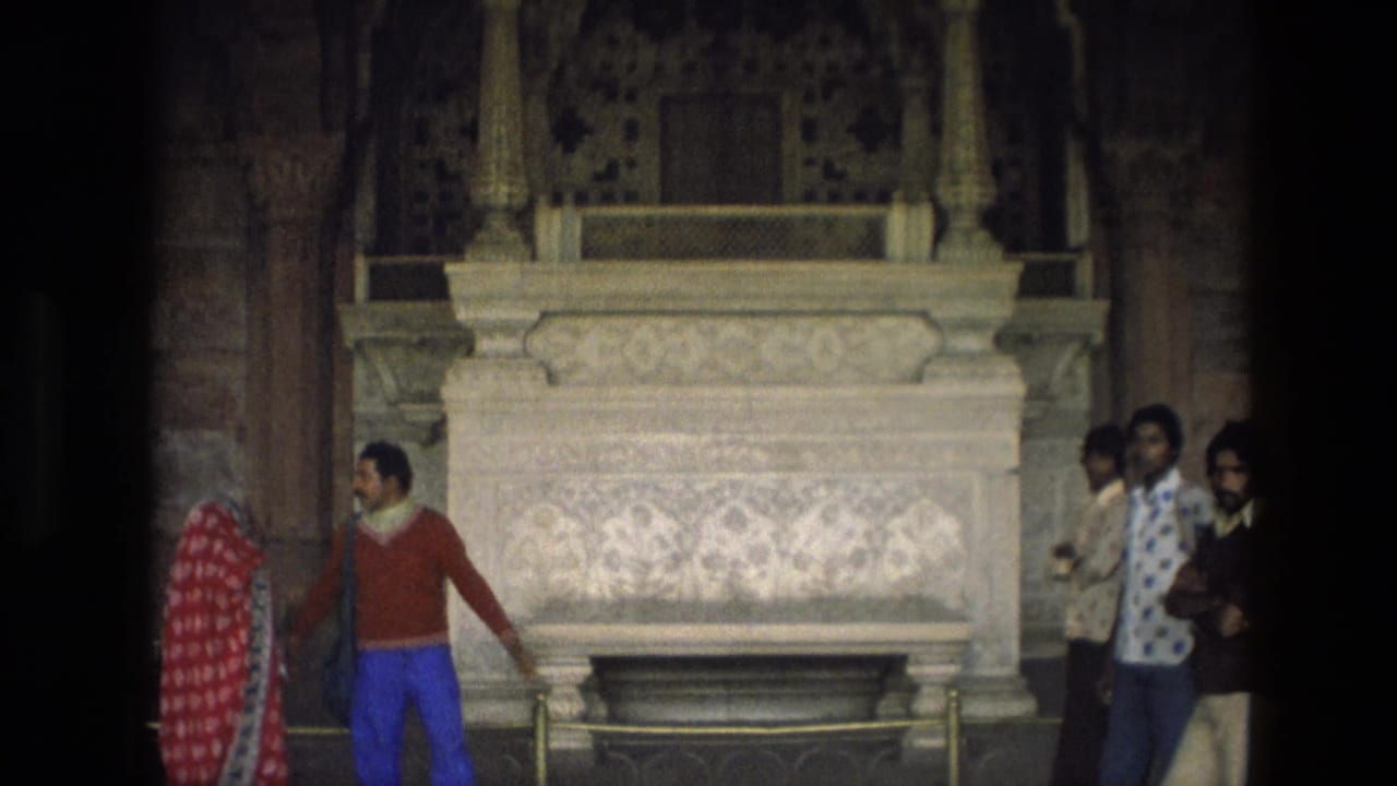 Visitors stand inside a temple near an ornate carved marble shrine or tomb.