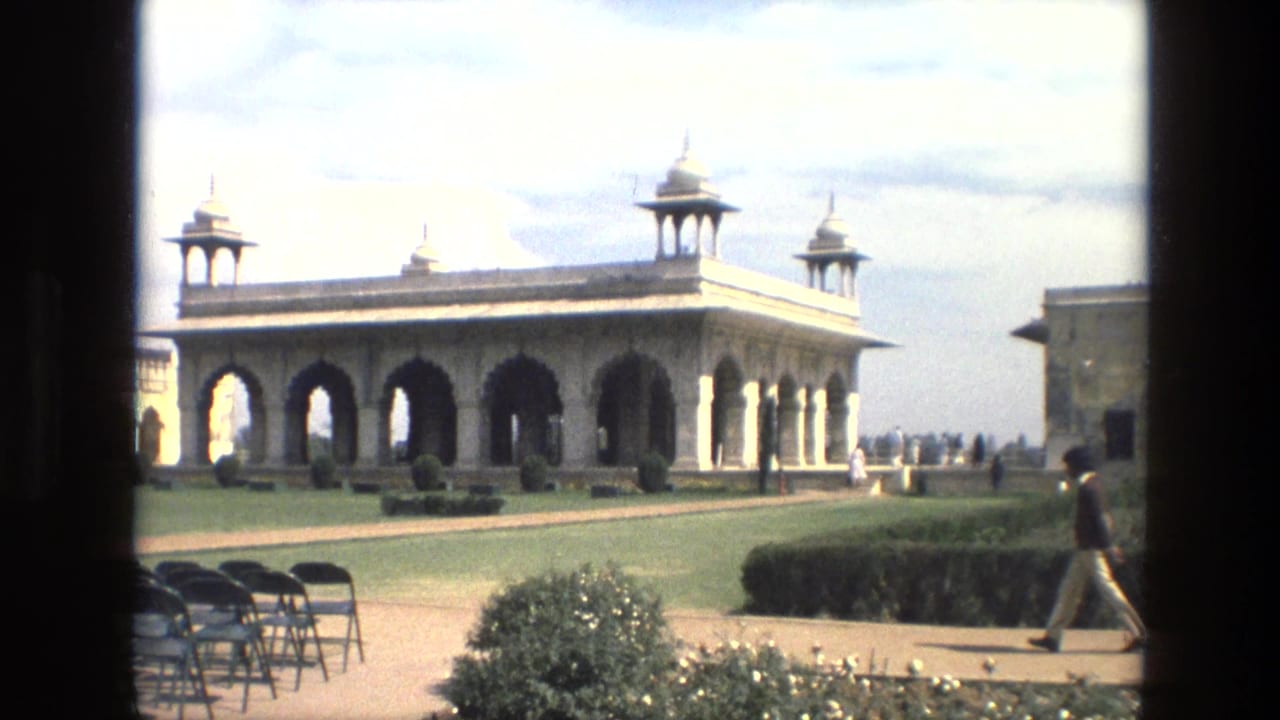 1974 India exterior view of a Mughal-style pavilion with arches, domed turrets, lawns, folding chairs, and visitors walking nearby.