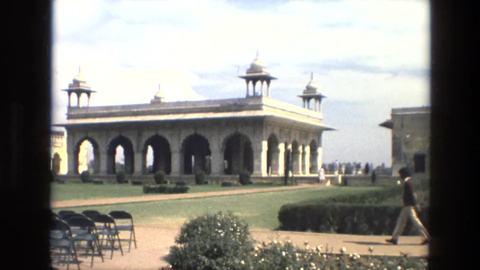 1974 India exterior view of a Mughal-style pavilion with arches, domed turrets, lawns, folding chairs, and visitors walking nearby.