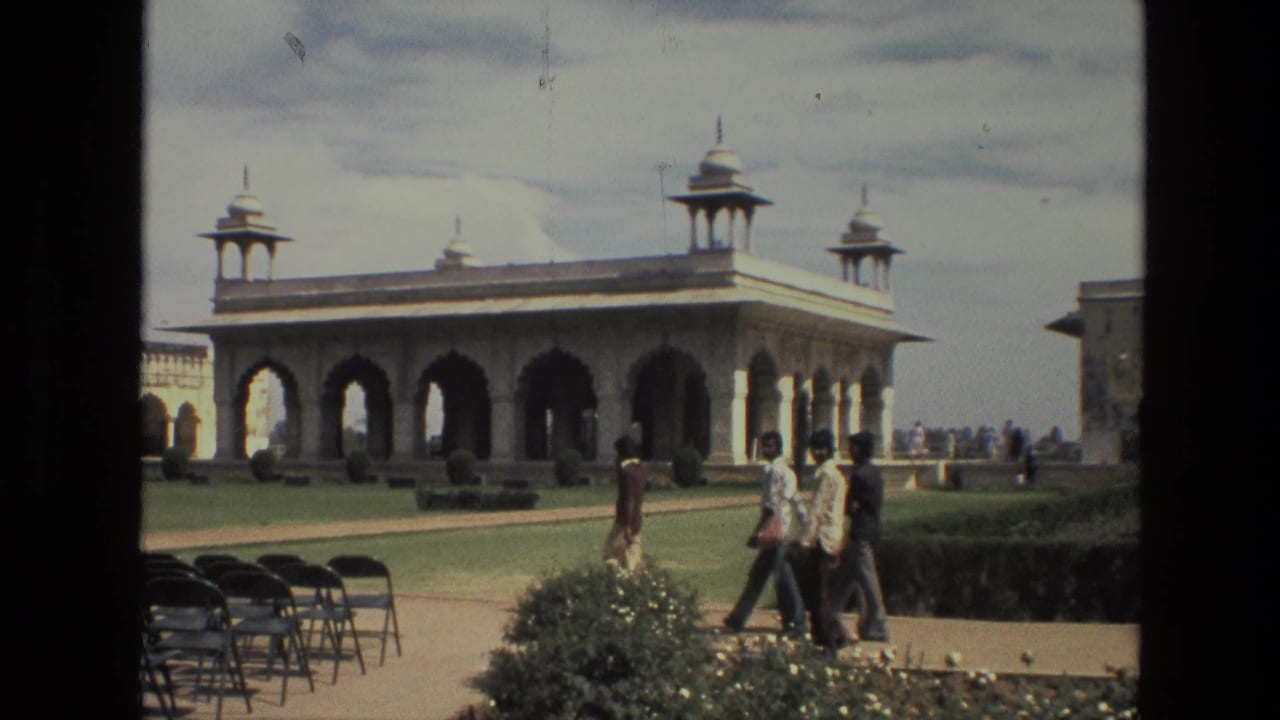 Visitors walk across a courtyard near an arched pavilion with domed roof features.