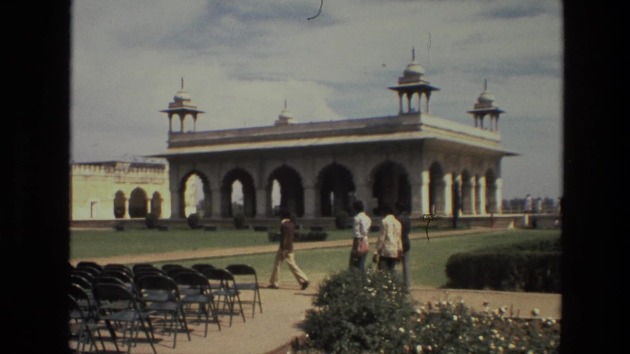 People walk through a landscaped courtyard in front of a large arched pavilion.