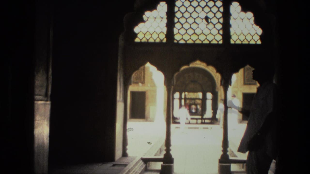 Shaded arched opening looking into a bright courtyard with latticework and a silhouetted figure.