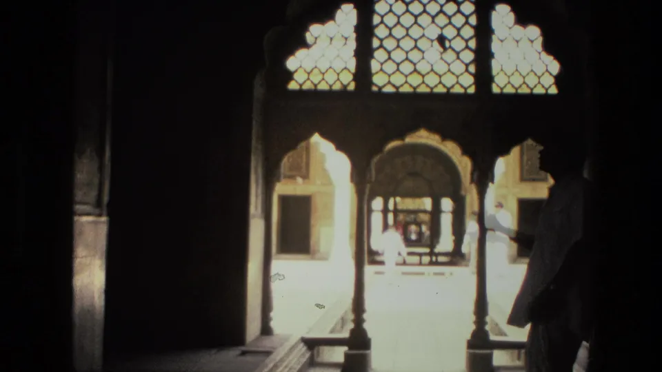 1974 India 8mm frame looking from a dark arcade through ornate arches into a sunlit courtyard with a figure near the right edge.