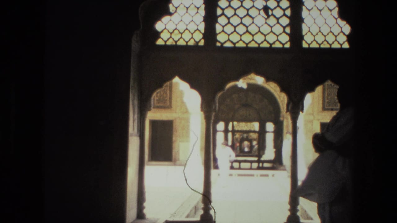 1974 India 8mm frame with ornate arched openings and a bright courtyard, with silhouetted visitors near the right edge.