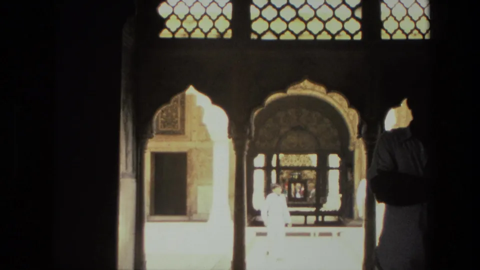 1974 India 8mm frame showing scalloped arches and latticework from a shaded passage, with visitors in and beyond the opening.