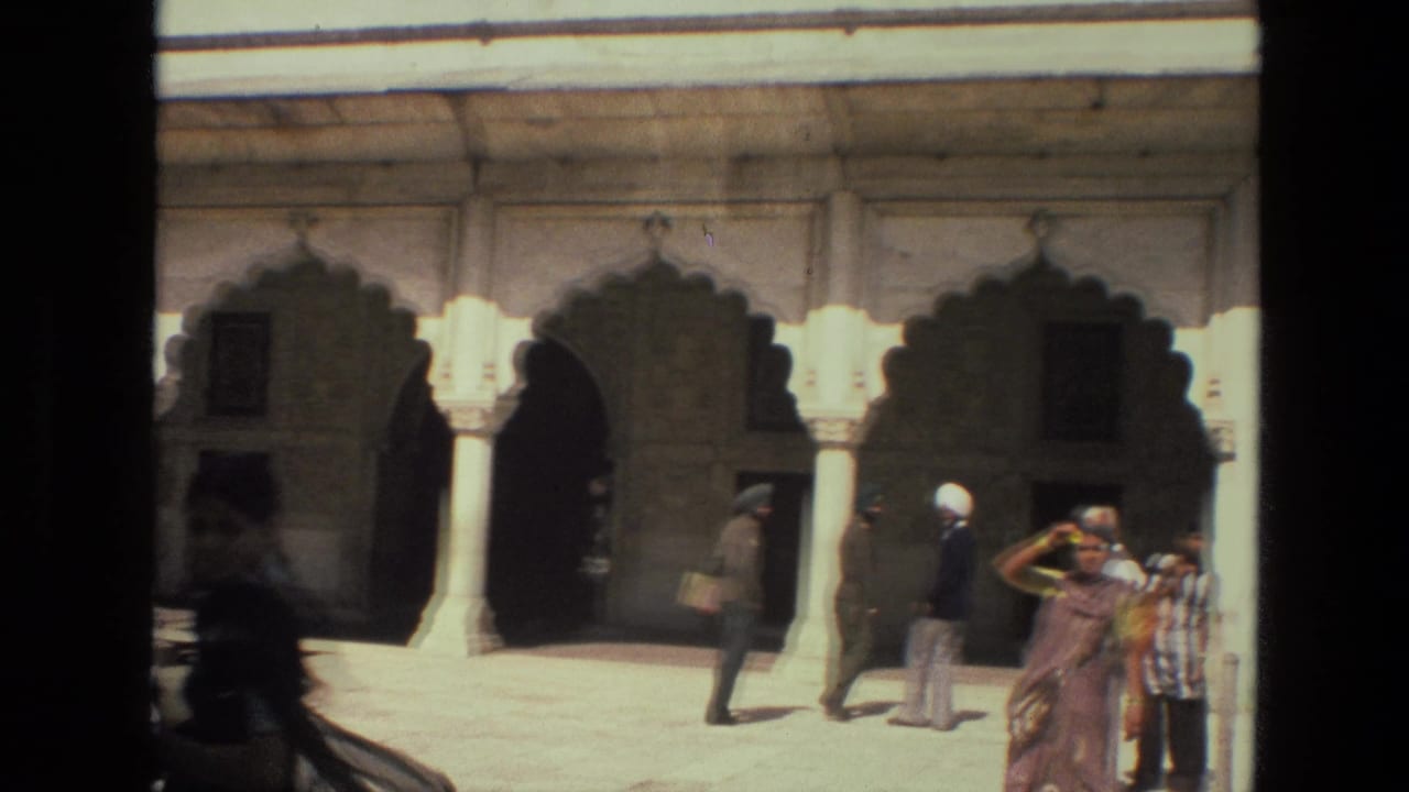 Visitors walk past scalloped palace arches and pale stone columns in a sunlit courtyard.