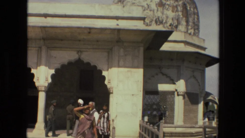 1974 India home-movie view of visitors near a palace corner, scalloped archways, columns, and a railing at the edge of the courtyard.