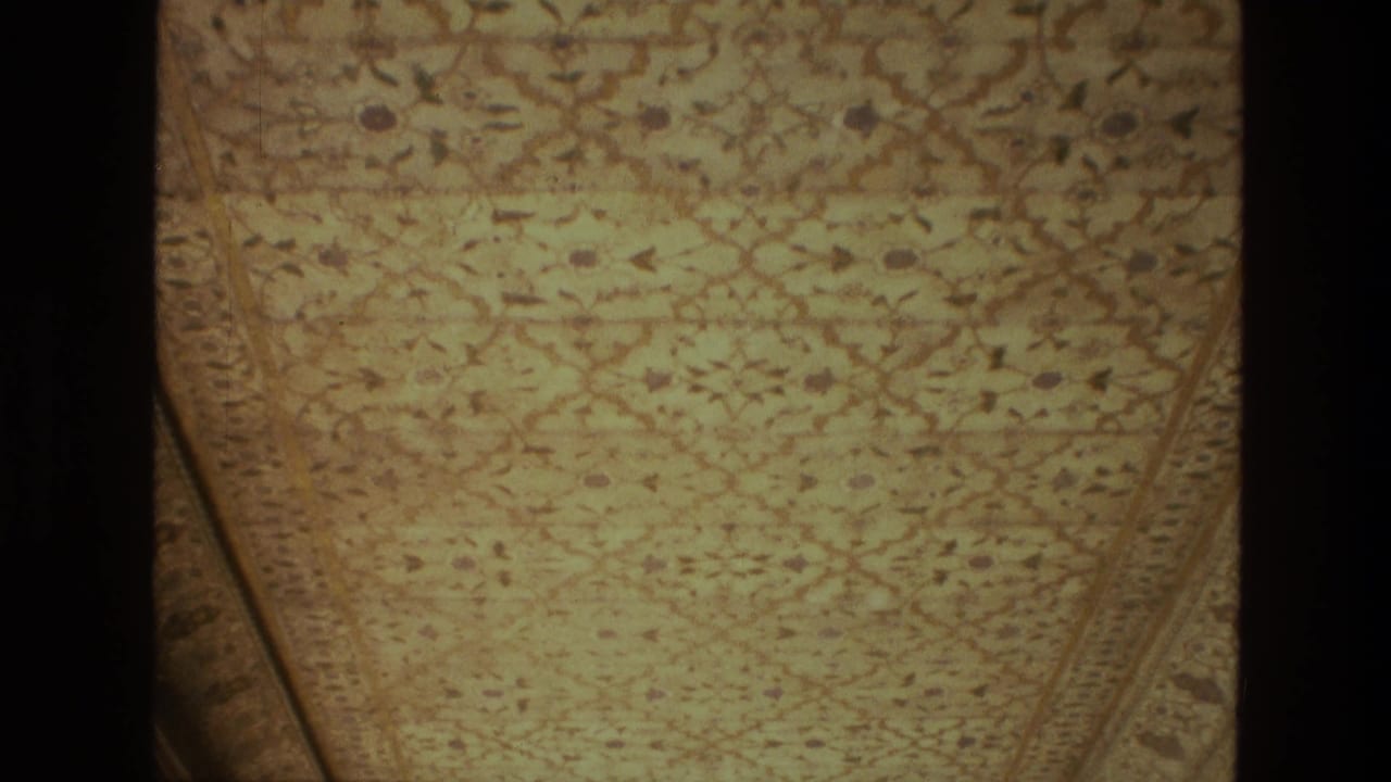 1974 India home-movie frame of a decorated ceiling section with repeating motifs, bordered edges, and visible film-strip division.