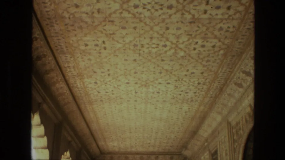 1974 India home-movie frame showing a longer upward view of an ornate ceiling with border panels and sunlight at the bottom edge.