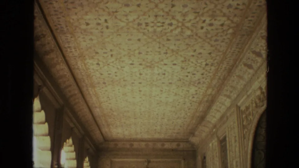 1974 India 8mm frame showing an ornate palace corridor ceiling, arched side openings, carved walls, and dark film borders.