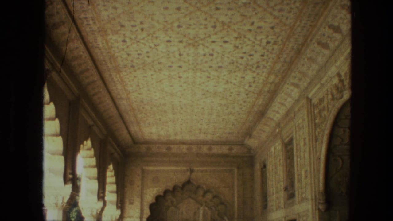1974 India 8mm frame revealing more of the ornate corridor, including carved wall panels, arched openings, and a scalloped doorway ahead.