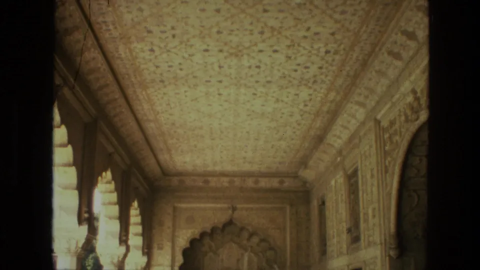 1974 India 8mm frame revealing more of the ornate corridor, including carved wall panels, arched openings, and a scalloped doorway ahead.