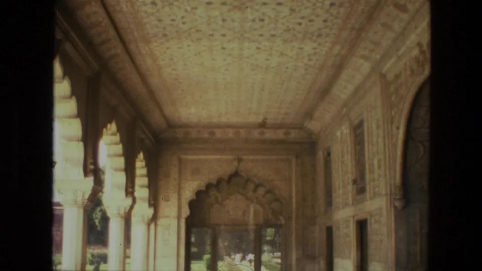 1974 India 8mm frame with the camera lower on the corridor, showing bright side arches, carved stonework, and a scalloped doorway at the end.