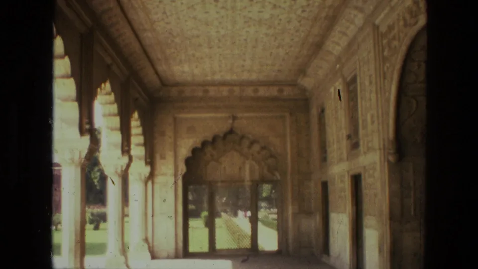 1974 India 8mm frame showing the lower portion of an ornate palace corridor, with a scalloped doorway, sunlit arches, and carved wall panels.