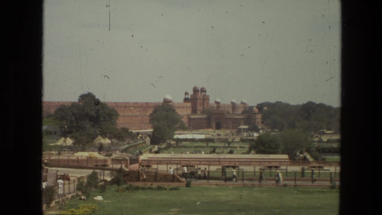 Distant red sandstone fortress beyond gardens and paths, seen through a dark film frame border.