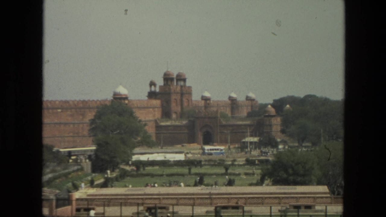 Red sandstone fort beyond gardens and a roadway, filmed from an elevated visitor viewpoint.
