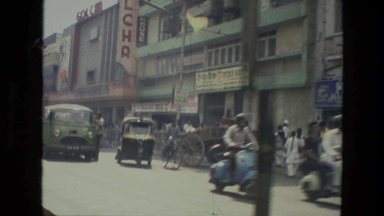 1974 Indian city street with mixed traffic, scooters, an auto-rickshaw, pedestrians, and Hindi storefront signage.