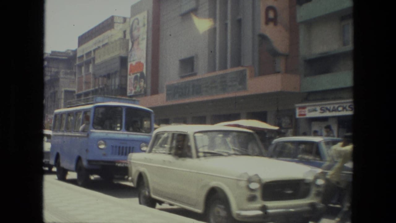 Blue bus and pale vintage car on a busy street beside shopfronts.