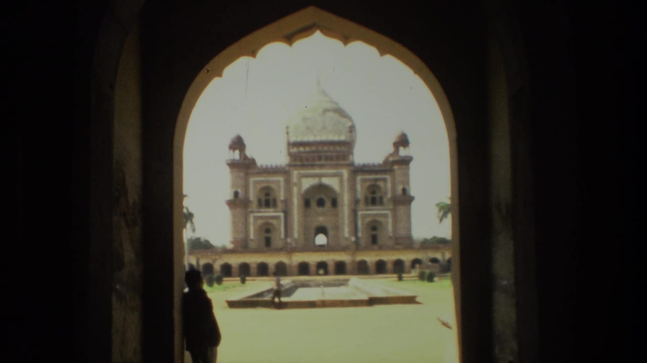 1974 India 8mm frame of a grand domed monument and courtyard viewed through a shaded arched gateway, with a visitor silhouette for scale.
