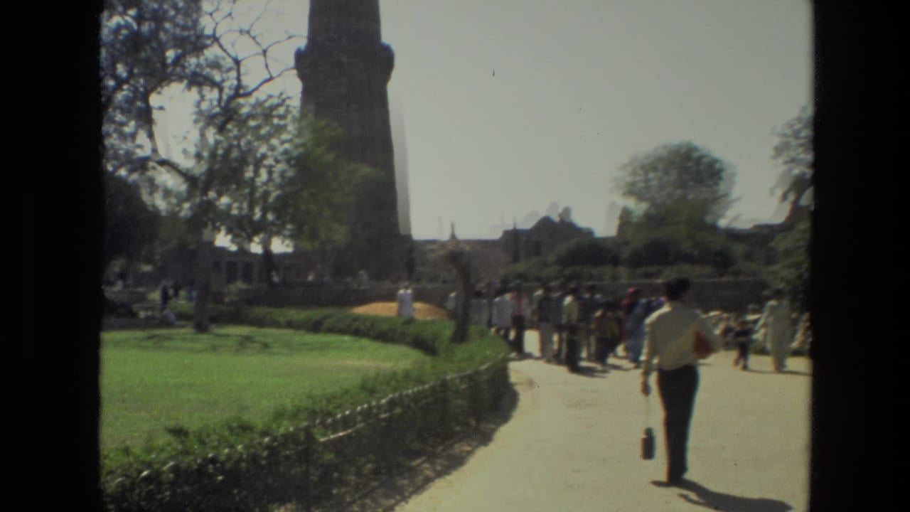 1974 home-movie view of visitors walking through landscaped grounds near the Qutub Minar in India.