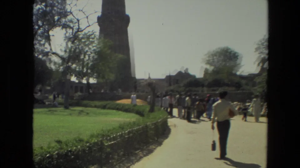 1974 home-movie view of visitors walking through landscaped grounds near the Qutub Minar in India.