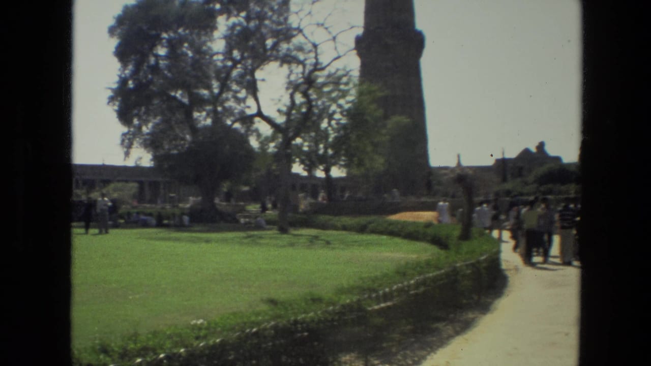 Landscaped grounds at the Qutub Minar complex with visitors crossing paths under bright daylight.