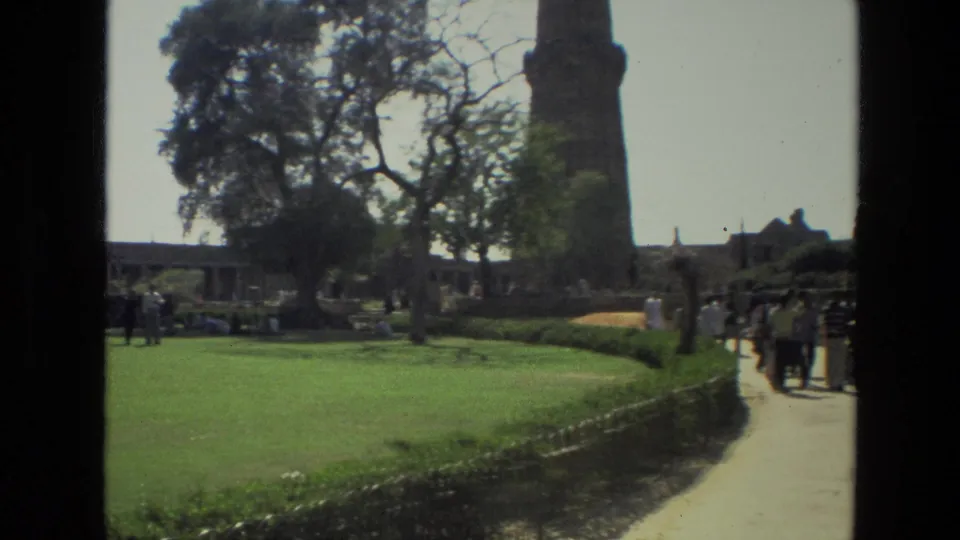 Landscaped grounds at the Qutub Minar complex with visitors crossing paths under bright daylight.