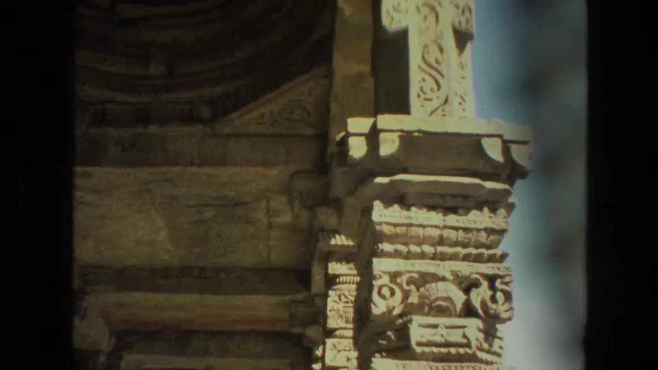 1974 8mm India frame showing carved temple pillars, weathered stonework, and deep shadows in an ancient ruin setting.