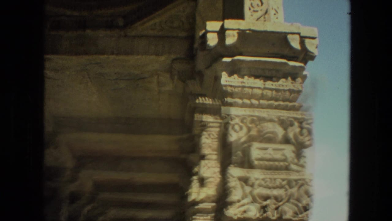 Close view of an ornate carved pillar beside blue sky and stone wall sections.