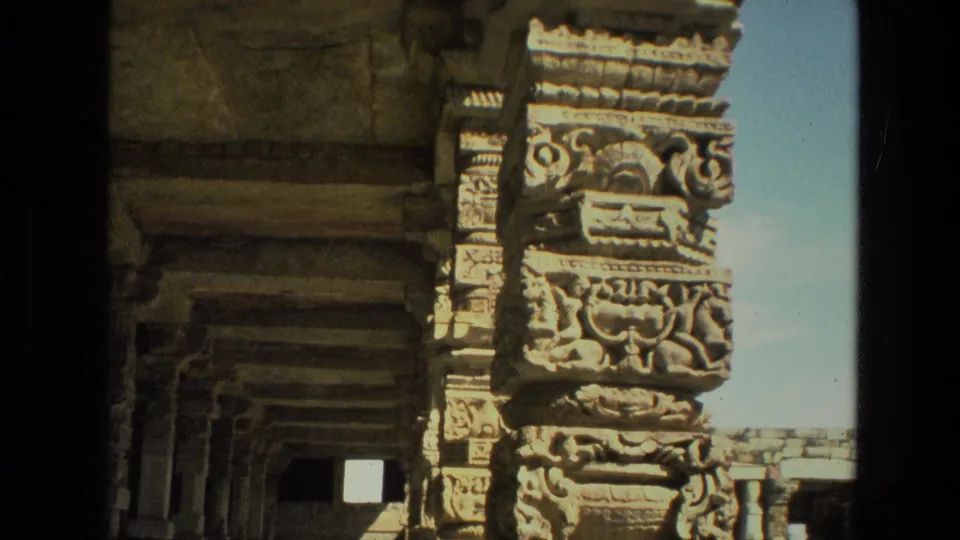 1974 8mm India frame showing an ornate temple column with shadowed colonnade space receding behind it.