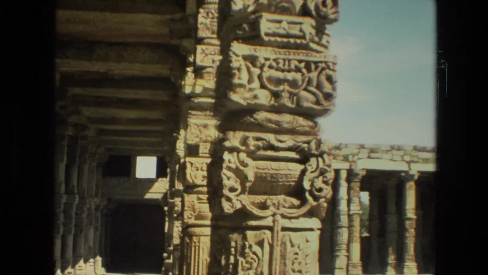 1974 India frame showing carved temple stonework, a dark opening, and remaining ruin walls under bright daylight.