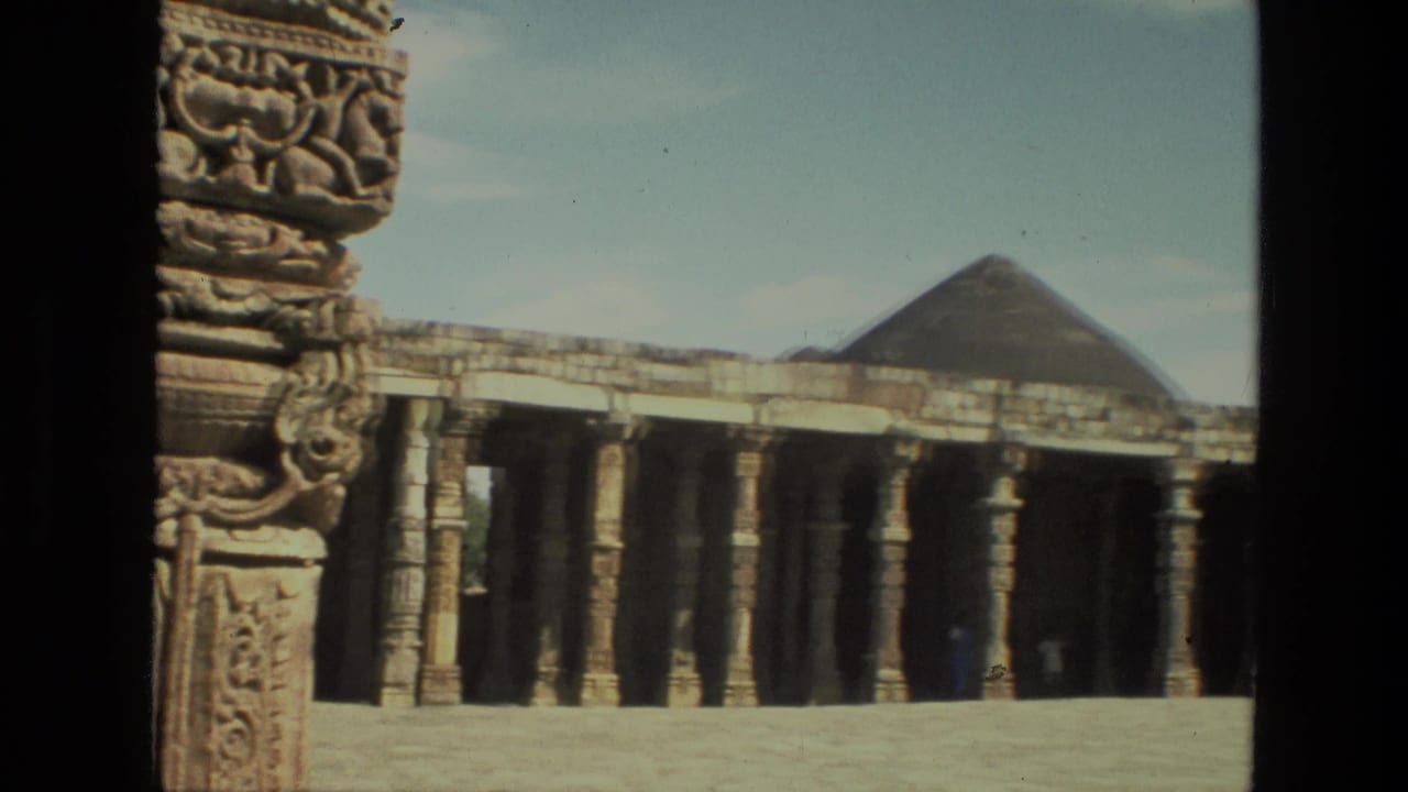 1974 India 8mm frame of a broad stone courtyard, repeated temple columns, and a pyramidal or domed roof form in the distance.