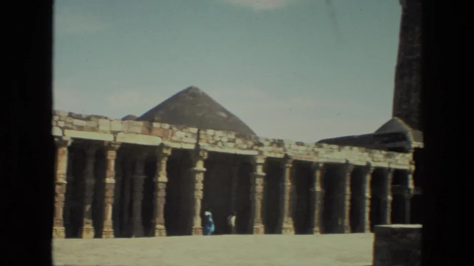 1974 India 8mm frame showing a temple colonnade across an open courtyard, with a distant visitor near the columns.