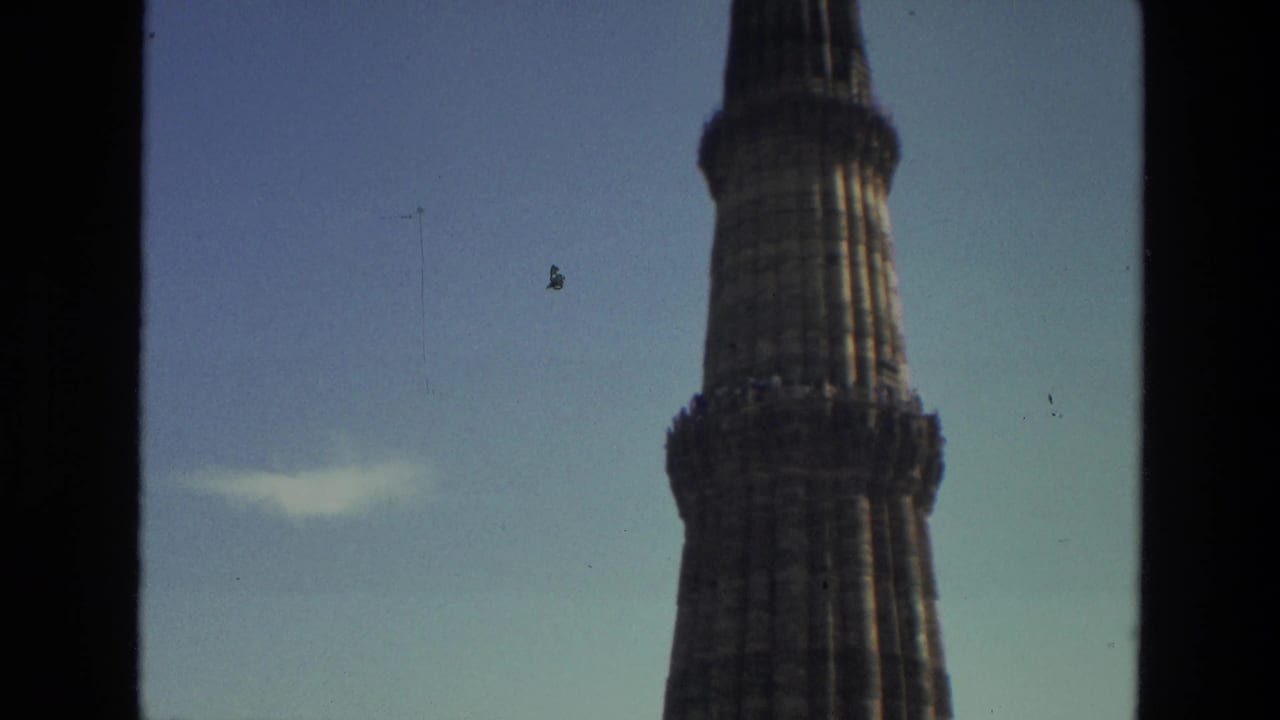 1974 8mm view of Qutub Minar in Delhi, showing the upper stone tower against a clear sky through dark frame edges.