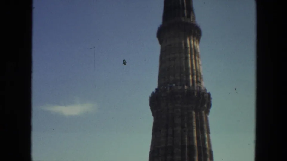 1974 8mm view of Qutub Minar in Delhi, showing the upper stone tower against a clear sky through dark frame edges.