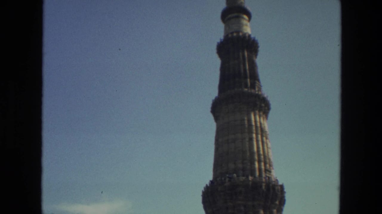 Upper section of Qutub Minar tower seen against clear sky with a dark vertical frame edge.