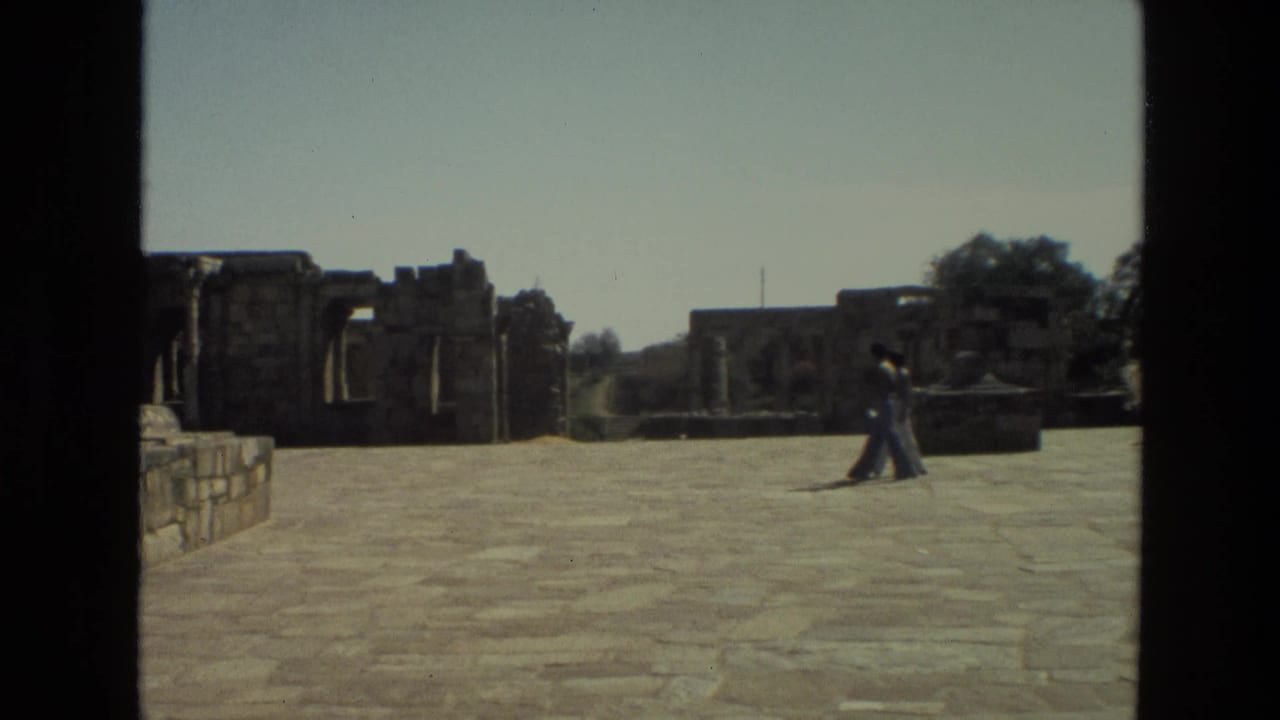 Visitors walk across a paved courtyard beside ancient stone ruins.