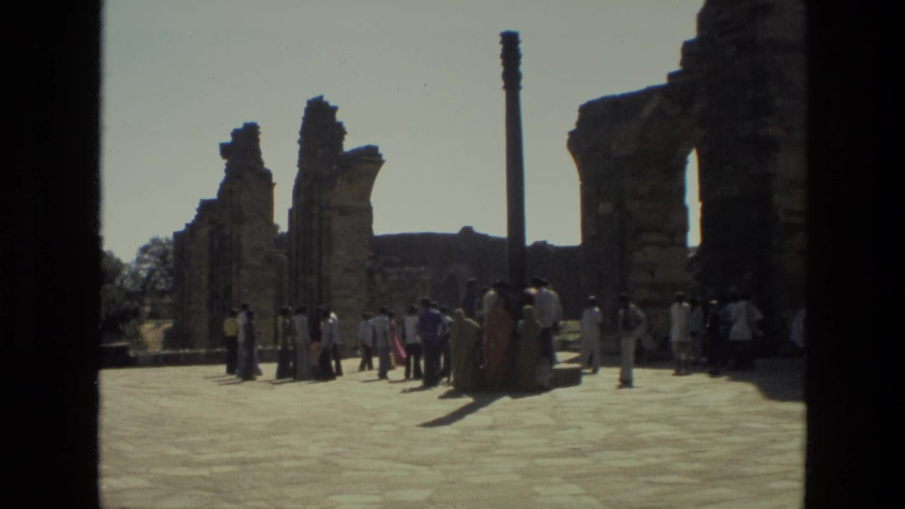 Tourists gather among stone ruins and tall pillars under a bright sky.