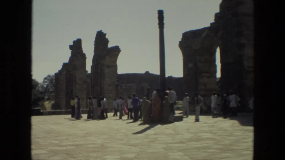 1974 8mm view of tourists standing and walking among weathered stone ruins at the Qutub Minar complex in India.