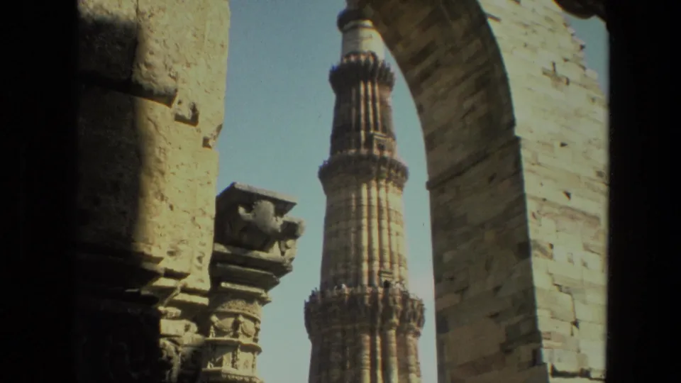 The Qutub Minar rises beyond a large stone arch in 1974 8mm travel footage from Delhi, India.