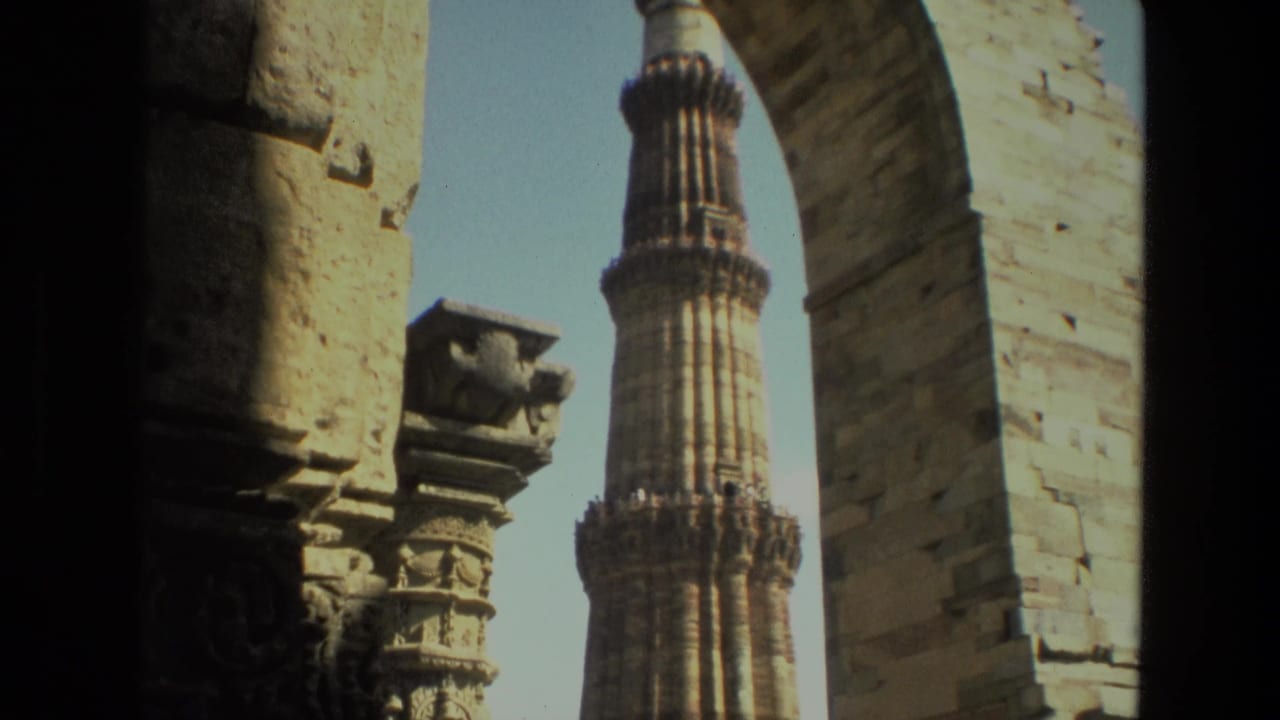 1974 8mm view of Qutub Minar in Delhi framed by shadowed stone arches and carved masonry.