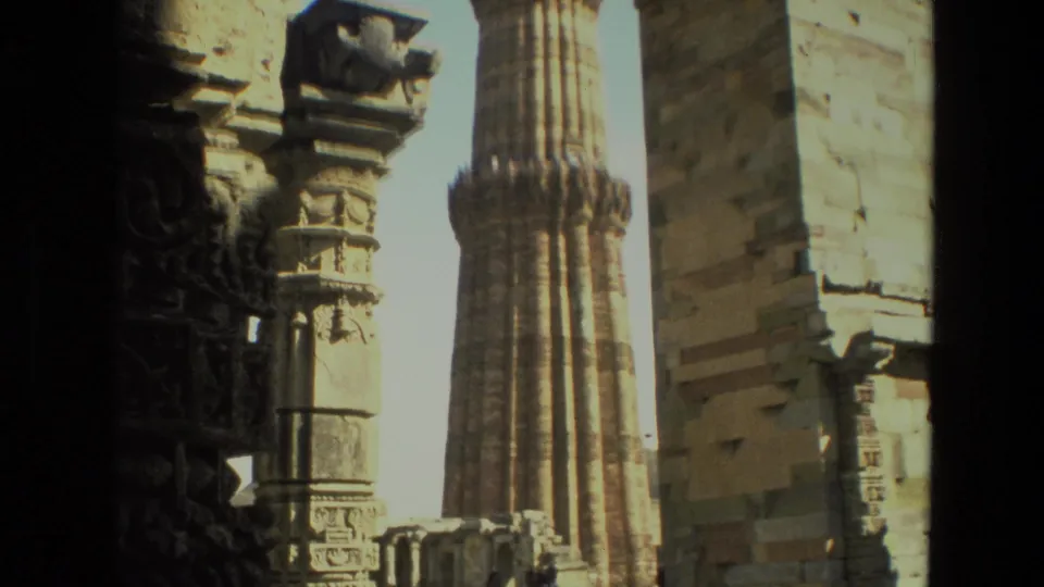 A 1974 Delhi monument view shows Qutub Minar through an arch, with carved stonework and a small ruin fragment below.