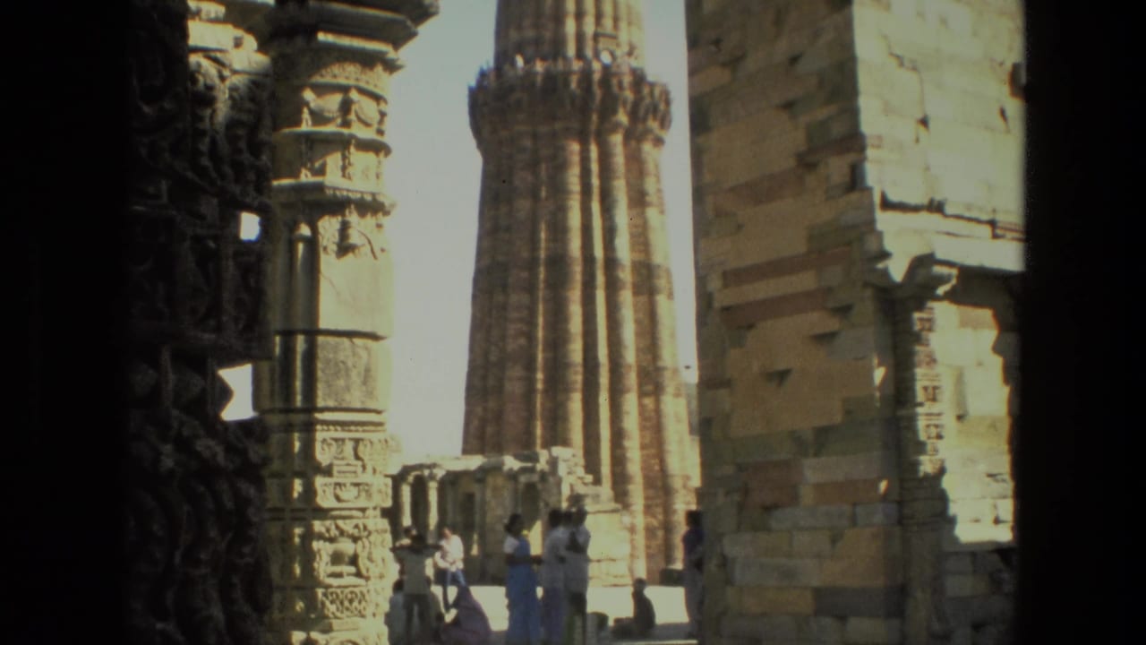Qutub Minar and adjacent stone structures with tourists gathered in sunlight.